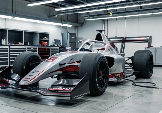 Monoplace de Formule 1 de nouvelle génération vu de trois quarts dans un stand moderne, avec ses ailerons actifs visibles et une ambiance technique réaliste.